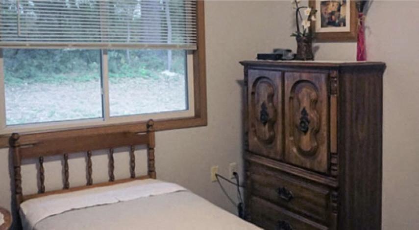 A bedroom with a bed, a wooden dresser, and a window.